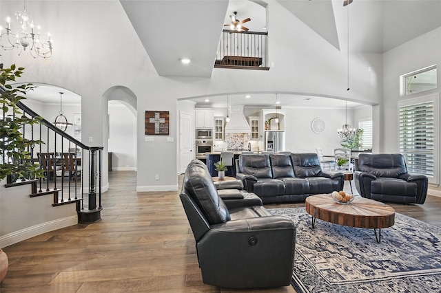 living area with stairway, wood finished floors, ceiling fan with notable chandelier, baseboards, and arched walkways