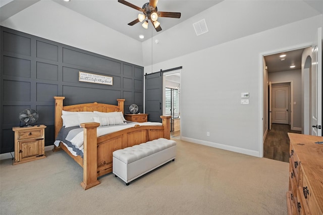 bedroom featuring vaulted ceiling, ceiling fan, a decorative wall, visible vents, and light carpet
