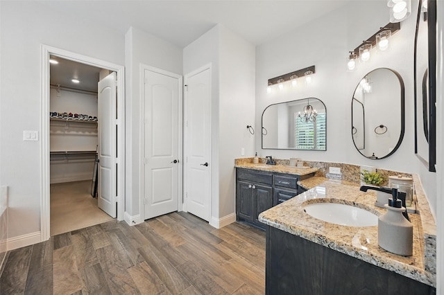 full bath featuring a notable chandelier, vanity, wood finished floors, a spacious closet, and baseboards