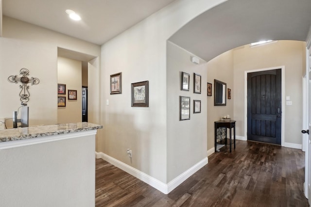 foyer with dark wood finished floors, baseboards, and arched walkways