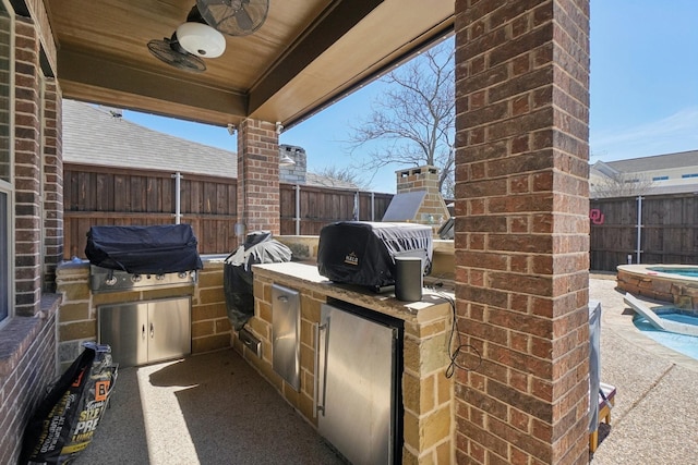 view of patio / terrace featuring a fenced backyard, a grill, an in ground hot tub, and exterior kitchen
