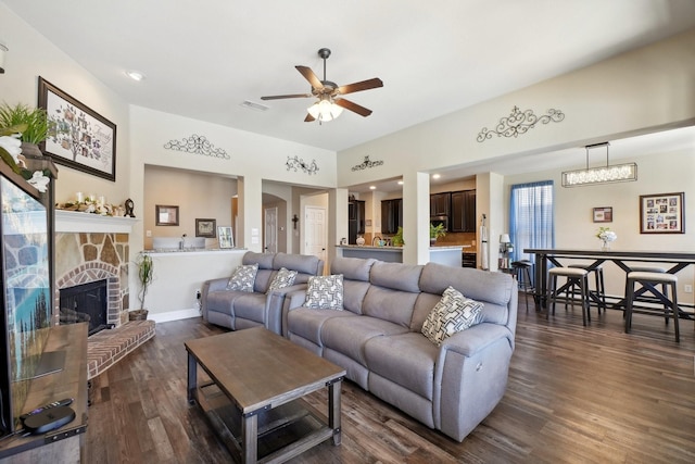 living room featuring dark wood finished floors, a stone fireplace, visible vents, and ceiling fan