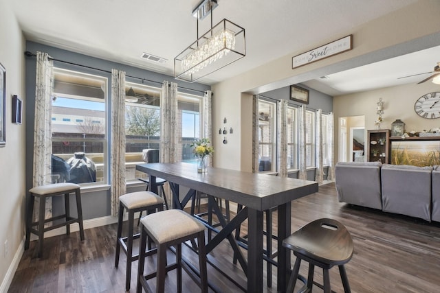 dining area with dark wood finished floors, baseboards, visible vents, and ceiling fan with notable chandelier