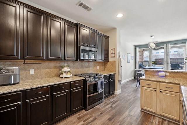 kitchen featuring visible vents, wood finished floors, tasteful backsplash, appliances with stainless steel finishes, and light stone counters