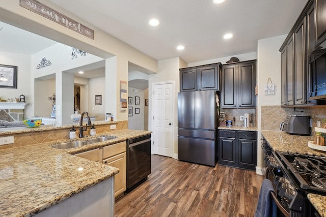 kitchen featuring tasteful backsplash, a sink, arched walkways, freestanding refrigerator, and black dishwasher