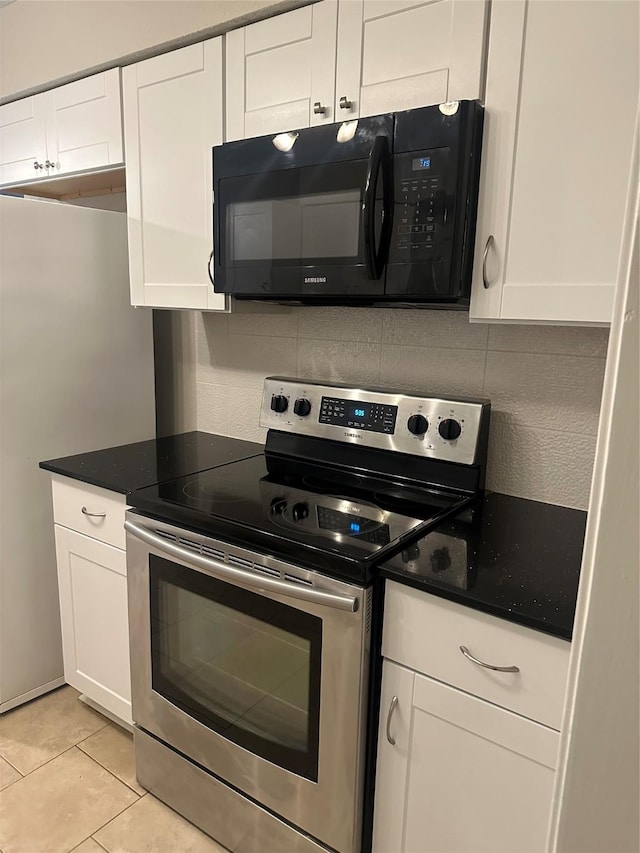 kitchen featuring tasteful backsplash, black microwave, light tile patterned floors, white cabinetry, and stainless steel range with electric cooktop