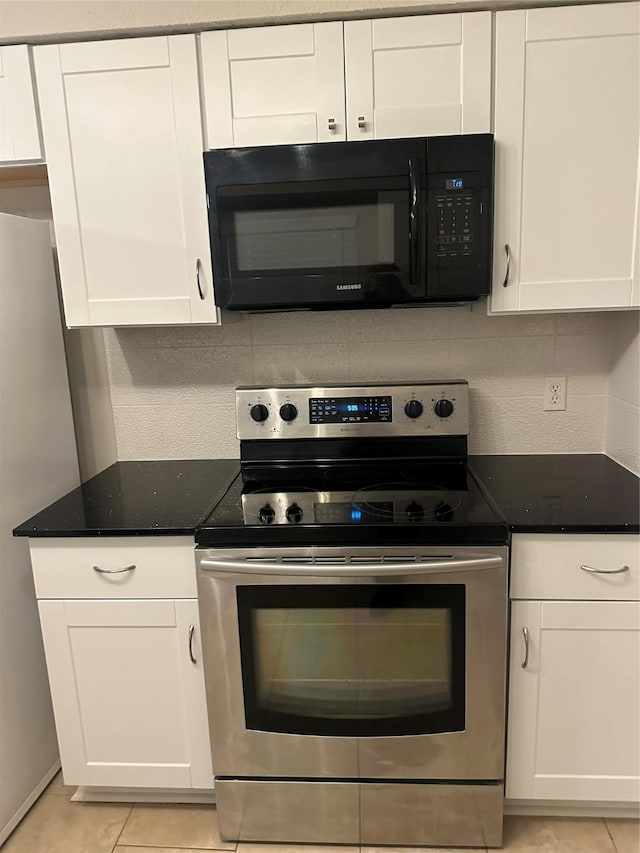 kitchen featuring dark stone counters, light tile patterned floors, white cabinetry, appliances with stainless steel finishes, and backsplash