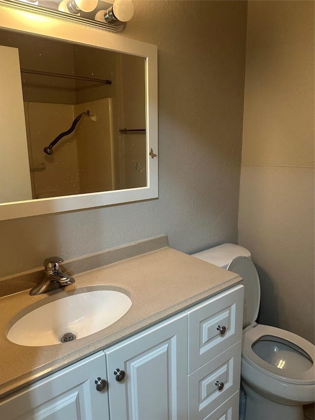 bathroom with toilet, vanity, and a textured wall