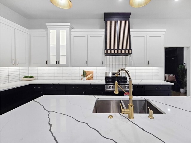 kitchen with range hood, light stone countertops, white cabinets, a sink, and decorative backsplash