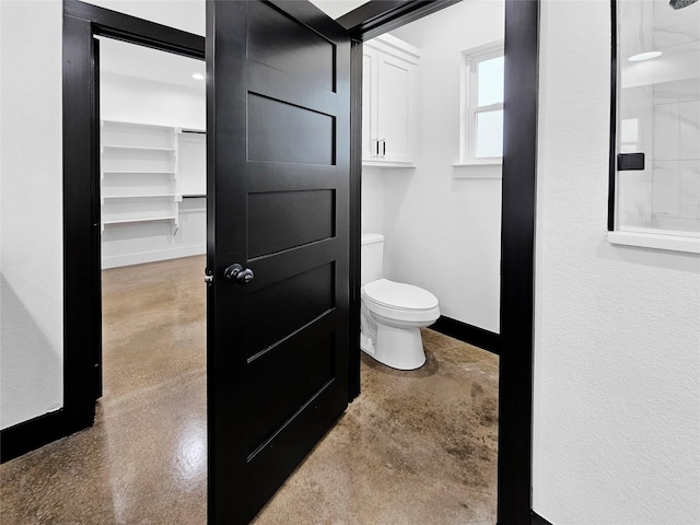 bathroom with toilet, finished concrete flooring, and baseboards