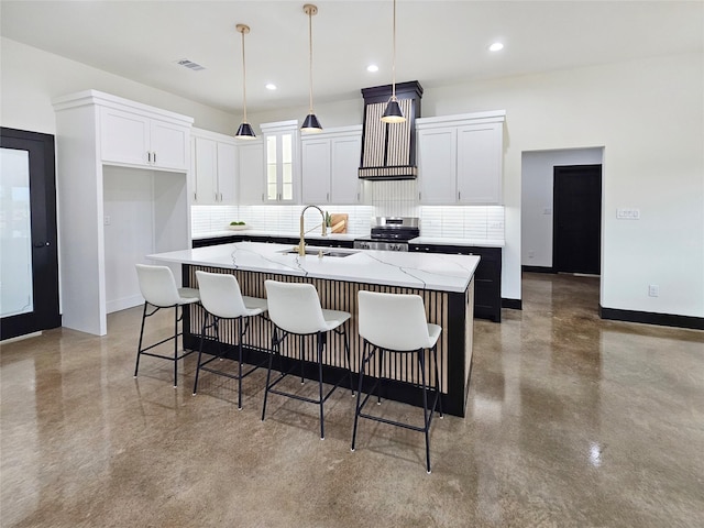 kitchen featuring visible vents, a sink, an island with sink, stainless steel range with electric cooktop, and decorative backsplash
