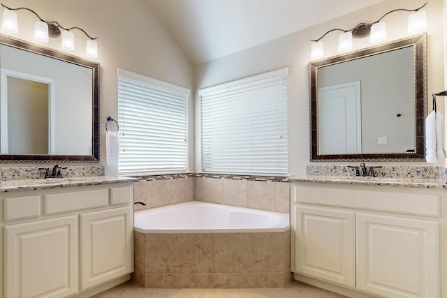 bathroom featuring a sink, two vanities, vaulted ceiling, and a garden tub