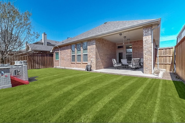 back of house featuring a shingled roof, a lawn, a fenced backyard, a patio, and brick siding