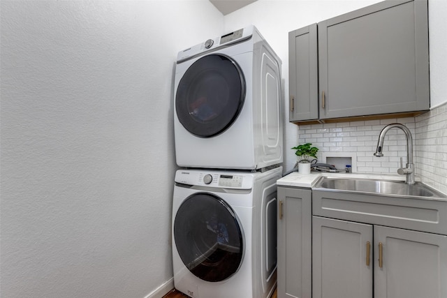 laundry area featuring cabinet space, stacked washer / dryer, and a sink