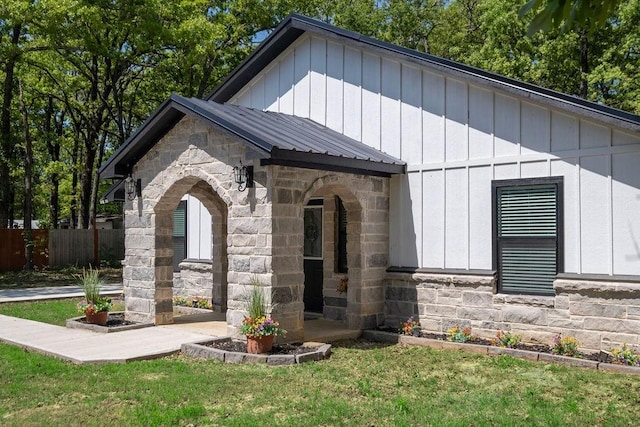 view of front of house featuring metal roof, fence, stone siding, and a front yard