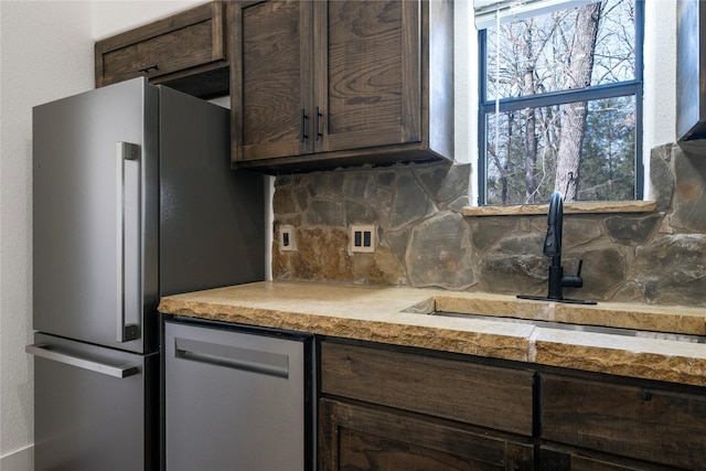 kitchen with light countertops, freestanding refrigerator, dark brown cabinets, backsplash, and a sink