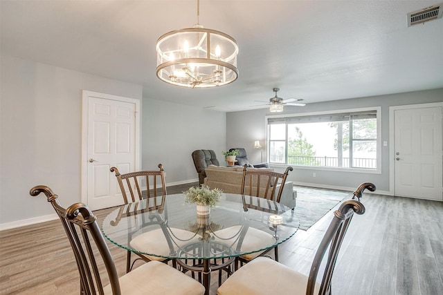 dining area featuring visible vents, light wood finished floors, baseboards, and ceiling fan with notable chandelier