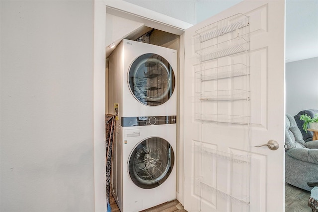 washroom featuring stacked washer / drying machine, wood finished floors, and laundry area