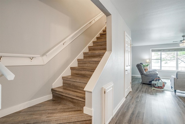 stairway with wood finished floors, a ceiling fan, and baseboards