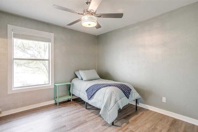 bedroom with light wood-type flooring, a ceiling fan, and baseboards