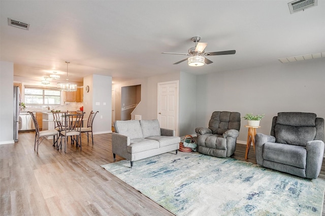 living room with ceiling fan with notable chandelier, baseboards, visible vents, and light wood-type flooring