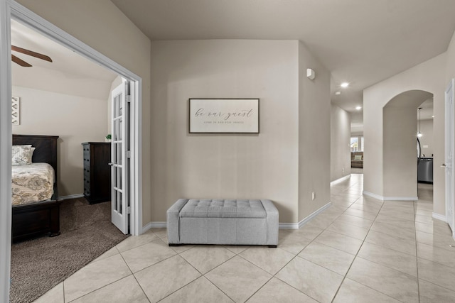 hall featuring arched walkways, baseboards, and light tile patterned floors