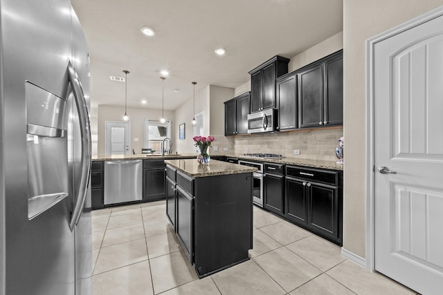 kitchen featuring light stone countertops, a peninsula, a center island, stainless steel appliances, and dark cabinets