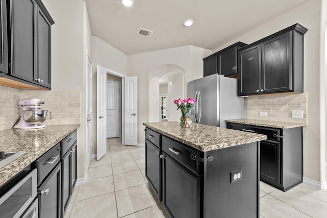 kitchen with a kitchen island, arched walkways, visible vents, freestanding refrigerator, and dark cabinets
