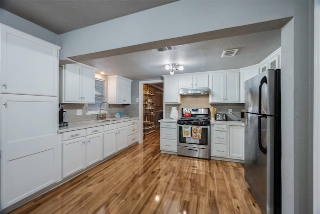 1112 Berkley Ave, Dallas, TX 75224 - kitchen with appliances with stainless steel finishes, under cabinet range hood, a sink, light countertops, and a textured ceiling