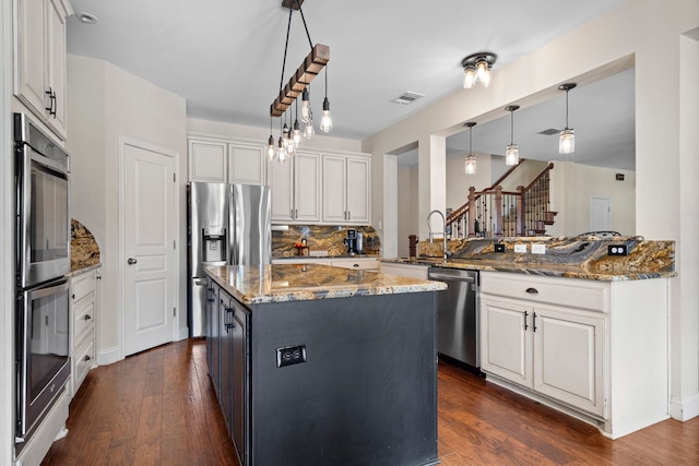 kitchen with white cabinets, appliances with stainless steel finishes, stone countertops, and dark wood-type flooring