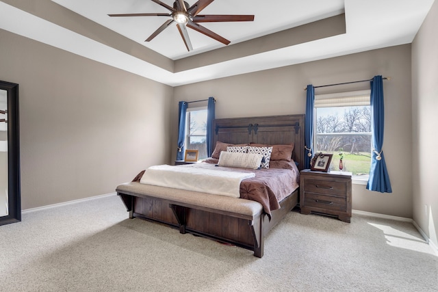 bedroom with baseboards, a tray ceiling, multiple windows, and light colored carpet