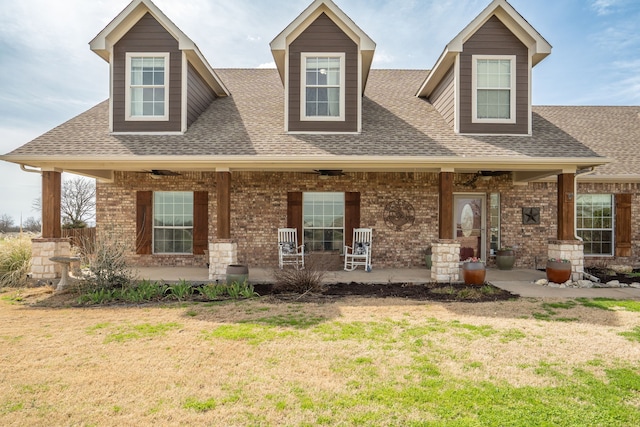 view of front facade with a front yard, a shingled roof, and covered porch