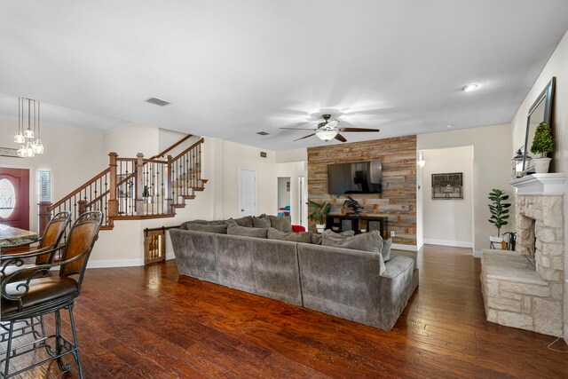 living area featuring stairs, a fireplace, dark wood finished floors, ceiling fan with notable chandelier, and visible vents