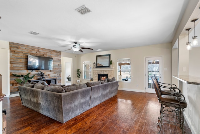 living area featuring dark wood-style flooring, ceiling fan, a fireplace, and visible vents
