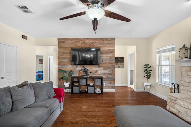 living area featuring baseboards, dark wood finished floors, ceiling fan, visible vents, and a stone fireplace