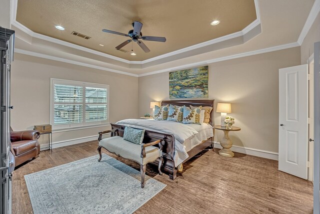 bedroom with baseboards, visible vents, wood finished floors, and a raised ceiling