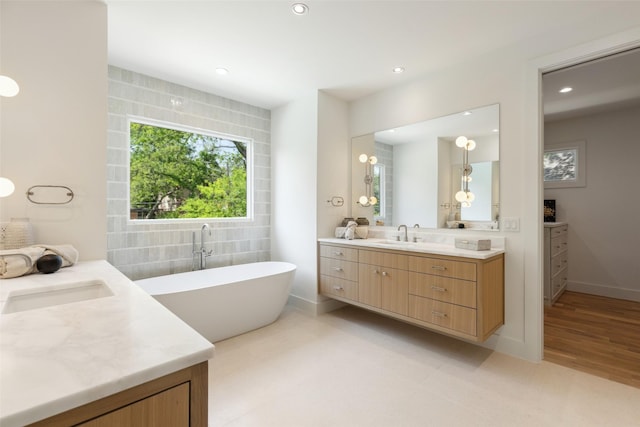 full bathroom featuring a freestanding tub, two vanities, a sink, baseboards, and recessed lighting