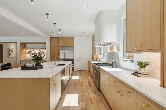 kitchen featuring high quality appliances, a sink, light brown cabinets, light wood-style flooring, and a large island with sink