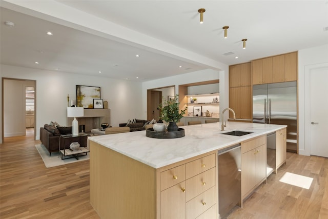 kitchen with a center island with sink, light wood-type flooring, a sink, light stone counters, and light brown cabinets