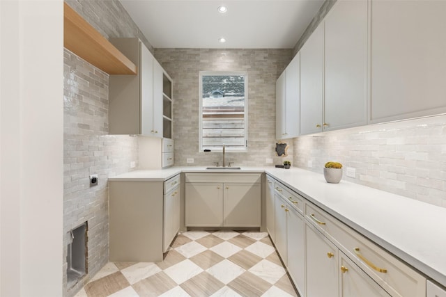 kitchen featuring open shelves, a sink, backsplash, and light countertops