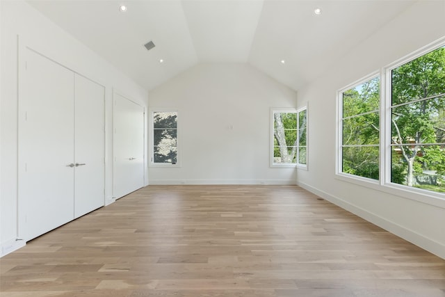 unfurnished bedroom featuring visible vents, light wood-style flooring, baseboards, and vaulted ceiling