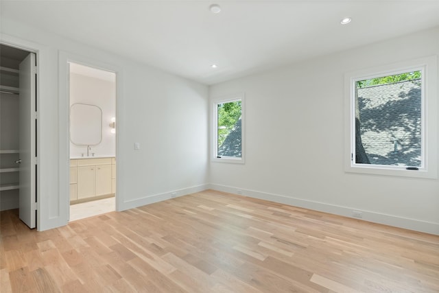 unfurnished bedroom with light wood-type flooring, a sink, baseboards, and a walk in closet