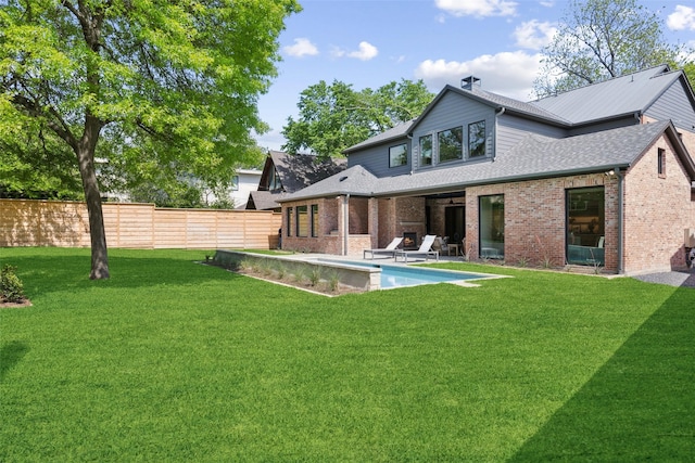 back of house featuring fence, brick siding, a fenced in pool, a patio area, and a lawn