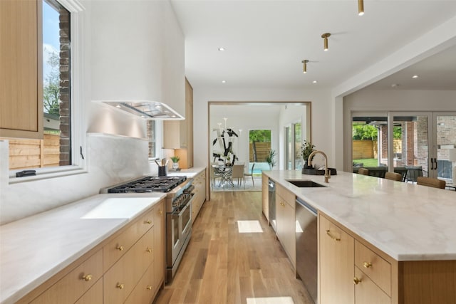 kitchen with light brown cabinetry, appliances with stainless steel finishes, light stone counters, a sink, and light wood-style flooring