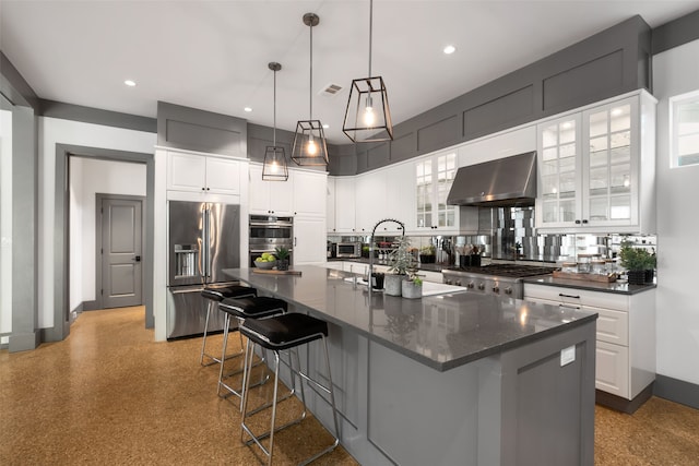 kitchen with an island with sink, wall chimney exhaust hood, decorative backsplash, and appliances with stainless steel finishes