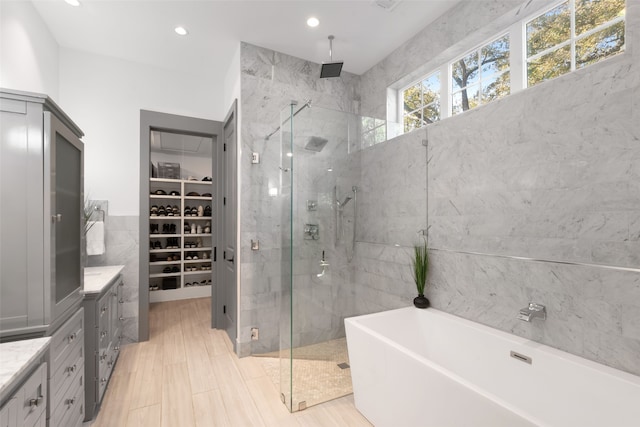 bathroom with tile walls, a walk in closet, a soaking tub, and a shower stall