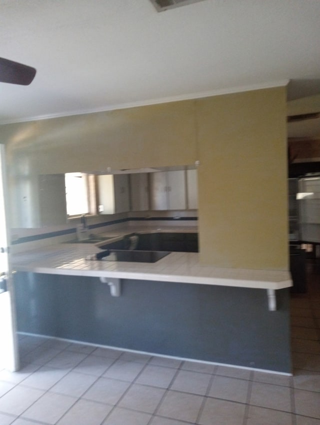 kitchen with tile patterned flooring, ornamental molding, and a kitchen bar