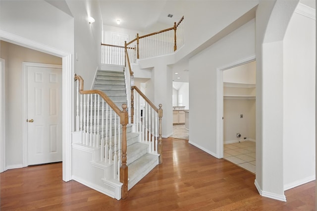 staircase with baseboards, visible vents, wood finished floors, and a towering ceiling