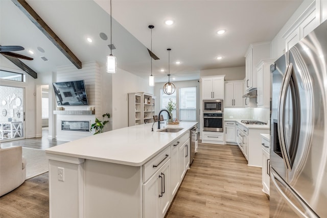 kitchen featuring decorative backsplash, appliances with stainless steel finishes, a sink, light wood-style floors, and open floor plan
