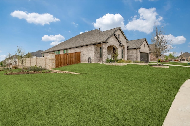 view of side of home with fence, an attached garage, brick siding, roof with shingles, and a lawn